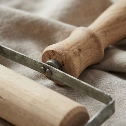 A manual wooden rolling pin and dough sheeter with a handle for rolling out large pastries.
